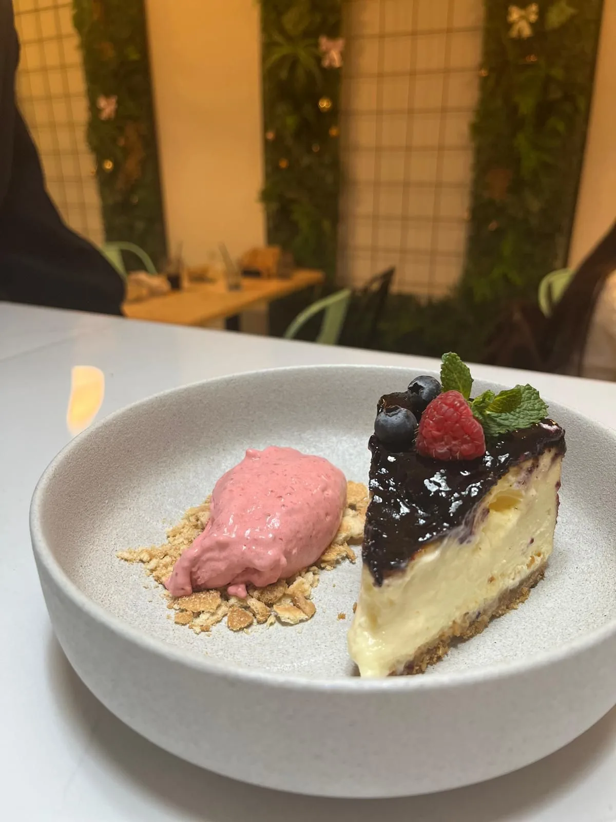 Porción de tarta de queso con salsa de frutos rojos y crema rosa servida en Nomada Restaurant & Brunch en Figueres